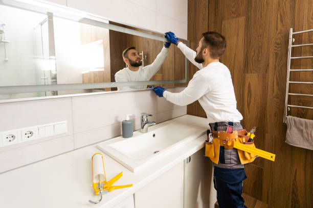The worker installs the mirror in the bathroom